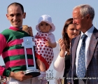 Federico Bossa con in braccio sua figlia, ha appena ricevuto la coppa per la vittoria del Gran Premio di Milano 2014 dall'ex grande fantino Vittorio Camici.