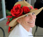 Un'affascinante proprietaria in Tribuna indossa un cappello con decorazioni floreali rosse 
